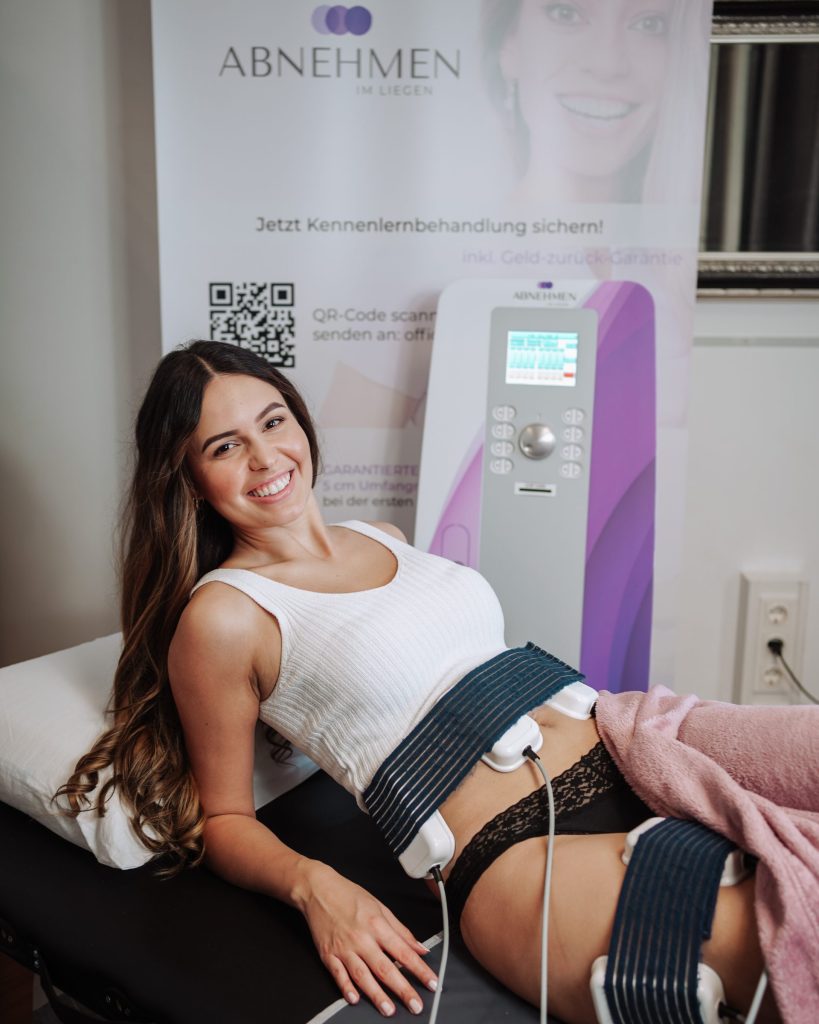 Eine Frau entspannt sich auf einem Massagetisch, während sie ein elektrisches Gerät zur Massage oder Behandlung verwendet.