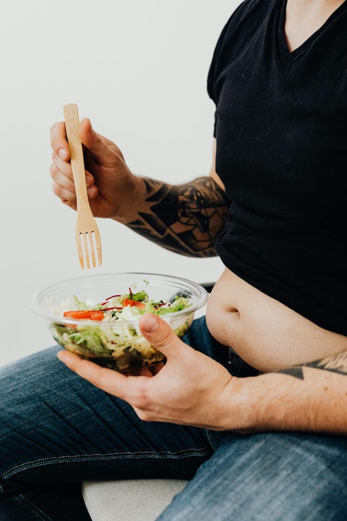 Person holding a bowl of salad with visible tattoos, highlighting healthy eating with personal style.